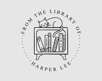 May include: A circular black and white stamp design featuring a cat resting on top of a small bookshelf filled with books. The text reads FROM THE LIBRARY OF and HARPER LEE in a circular border around the central illustration of the cat and shelf.