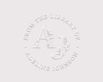 May include: A circular embossed stamp design on a light gray background featuring the letters AJ intertwined with delicate leaf illustrations. The text FROM THE LIBRARY OF and ADELINE JOHNSON is arranged in a circle around the central monogram.