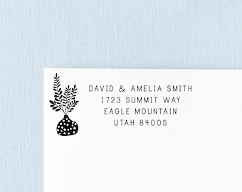 May include: A black ink return address stamp impression on white paper featuring a vase with a leafy plant and the text: DAVID & AMELIA SMITH, 1723 SUMMIT WAY, EAGLE MOUNTAIN, UTAH 84005. The design includes a dotted vase and a sprig of leaves.