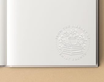 May include: A circular embossed stamp on a white page featuring a stack of three books topped with a teacup and floral sprigs. The text reads FROM THE LIBRARY OF EMILY BRONTE in a circular border around the central illustration.