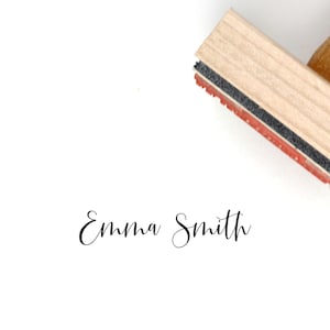 K&ouml;nnte beinhalten: Ein selbsttinte&shy;nder Stempel aus Holz mit einem schwarzen und roten Stempelkissen. Der Stempel tr&auml;gt die Aufschrift "Emma Smith" in kursiver Schrift.