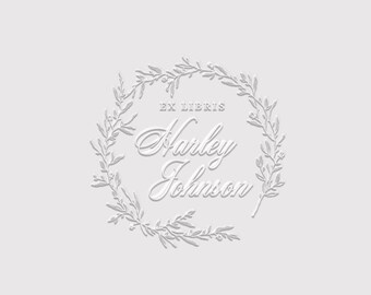 May include: A white embossed-style graphic design featuring a circular wreath of delicate leaves and branches. The text EX LIBRIS is centred at the top, followed by the name Harley Johnson in a cursive script font, all set against a light grey background.