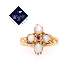May include: A gold-toned ring featuring a cross design. The ring has four white pearls and a central red gemstone. The ring's band has an ornate, swirling design. The image also includes a navy blue diamond-shaped logo with white text.