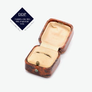 May include: A rectangular jewellery box with a brown and black mottled exterior finish. The interior is lined with beige velvet and features a central slot for a ring. The box has a hinged lid and a small metal latch on the front edge.