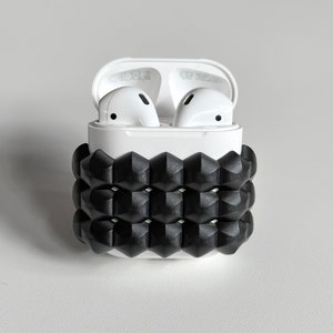 Puede incluir: Auriculares inalámbricos blancos en una caja de carga blanca con una funda de silicona negra pop-it.