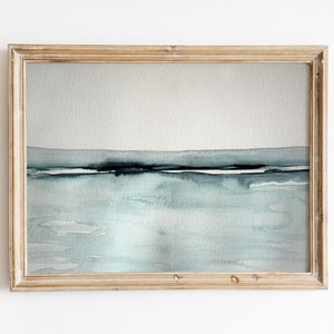 May include: A framed watercolor painting of a seascape with a light blue and gray color scheme. The painting depicts a horizon line with a thin band of dark blue and white, representing the water and sky.