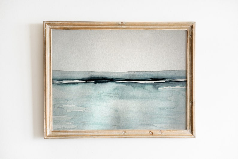 May include: A framed watercolor painting of a seascape with a light blue and gray color scheme. The painting depicts a horizon line with a thin band of dark blue and white, representing the water and sky.