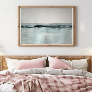 May include: A bedroom with a wooden bed frame and a pink and white checkered blanket. The bed has two pink pillows and a framed watercolor painting of a seascape above the headboard. Two gold pendant lights hang from the ceiling.
