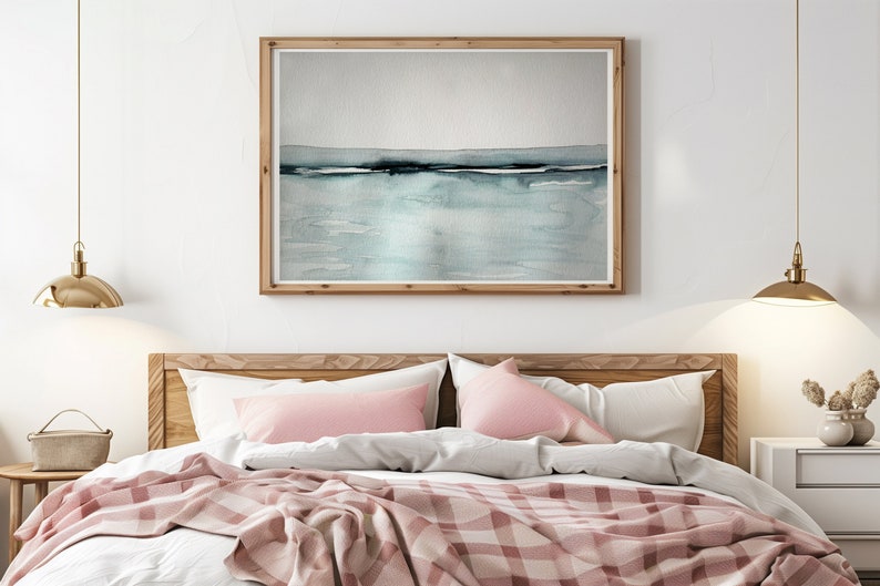 May include: A bedroom with a wooden bed frame and a pink and white checkered blanket. The bed has two pink pillows and a framed watercolor painting of a seascape above the headboard. Two gold pendant lights hang from the ceiling.