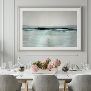 May include: A white dining table with six chairs, set for a meal. The table is decorated with a vase of pink flowers, two clear glass domes, and a glass bottle. A framed abstract watercolor painting of a seascape hangs on the wall behind the table.