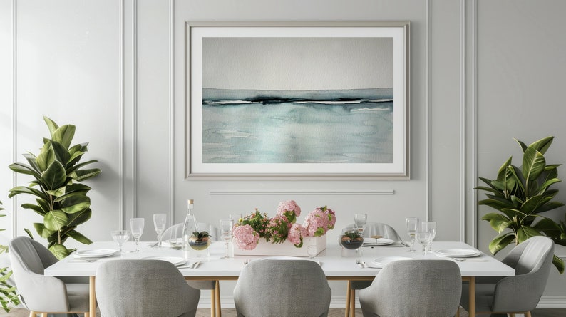 May include: A white dining table with six chairs, set for a meal. The table is decorated with a vase of pink flowers, two clear glass domes, and a glass bottle. A framed abstract watercolor painting of a seascape hangs on the wall behind the table.