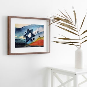 May include: A framed watercolor painting of a blue Star of David with a red, yellow, and blue background. The painting is in a brown frame and is hanging on a white wall.