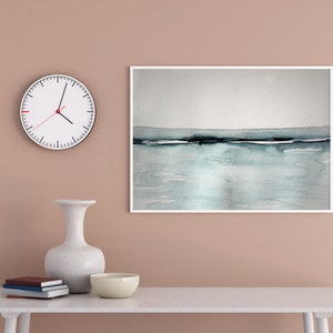 May include: A white clock with black hands and a red second hand hangs on a light brown wall above a white table. A white vase with a wide mouth sits on the table next to a white bowl. A framed watercolor painting of a blue and gray seascape hangs on the wall above the table.
