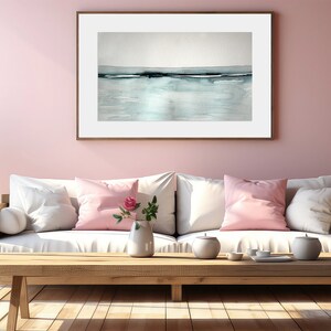May include: A white sofa with pink throw pillows sits in a living room with a light pink wall. A wooden coffee table sits in front of the sofa with a vase of pink flowers and a tea set. A framed abstract painting hangs on the wall above the sofa.