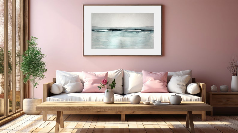 May include: A white sofa with pink throw pillows sits in a living room with a light pink wall. A wooden coffee table sits in front of the sofa with a vase of pink flowers and a tea set. A framed abstract painting hangs on the wall above the sofa.