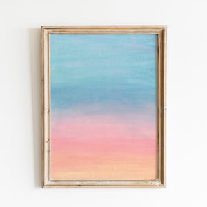 May include: A framed abstract painting with a gradient of blue, pink, and orange colours. The painting is in a light wood frame.