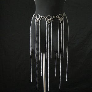 Könnte beinhalten: Ein silbernes Ketten-Bikini-Set auf einer schwarzen Schaufensterpuppe. Das Set umfasst ein Neckholder-Top, einen Choker und ein Taillenstück mit herabhängenden Ketten. Die Metallteile sind aufwendig miteinander verbunden.
