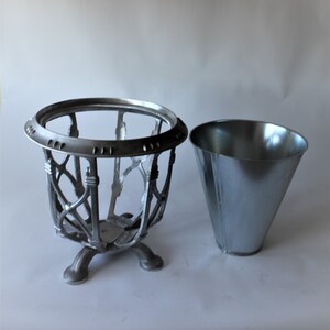 May include: A silver-coloured metal ice bucket with a decorative openwork design and a separate, matching cone-shaped container. The ice bucket has a round top and sits on three curved feet.