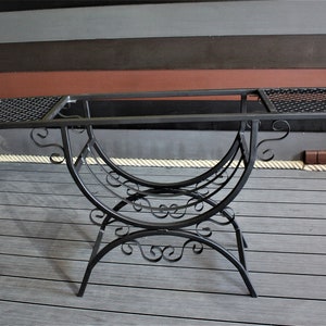 May include: Black metal table with a decorative, scrolled base and two rectangular tops with wire mesh inserts.