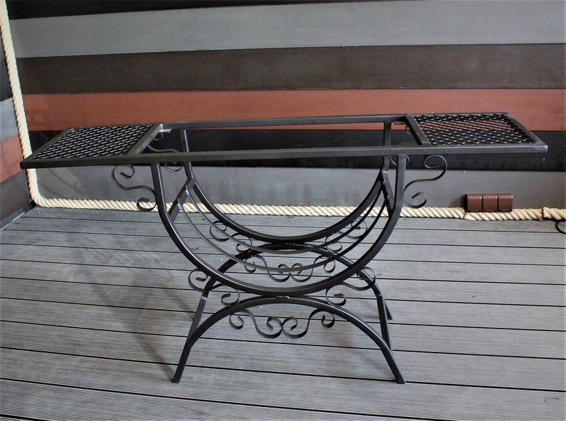 May include: Black metal table with a decorative, scrolled base and two rectangular tops with wire mesh inserts.