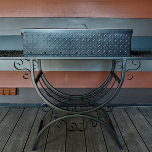 May include: Black metal grill with a diamond-plate lid and a decorative wrought iron stand. The grill is sitting on a wooden deck.