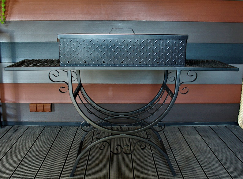 May include: Black metal grill with a diamond-plate lid and a decorative wrought iron stand. The grill is sitting on a wooden deck.