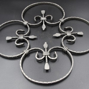 Puede incluir: Una pieza decorativa de arte mural de metal con un diseño simétrico. Cuatro elementos circulares están conectados por adornos estilizados. El metal tiene un acabado oscuro y mate, probablemente de hierro forjado.