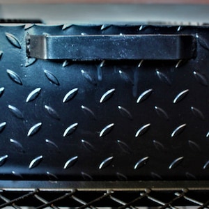 May include: Black metal box with a diamond plate pattern and a black handle. The box is sitting on a black metal frame.