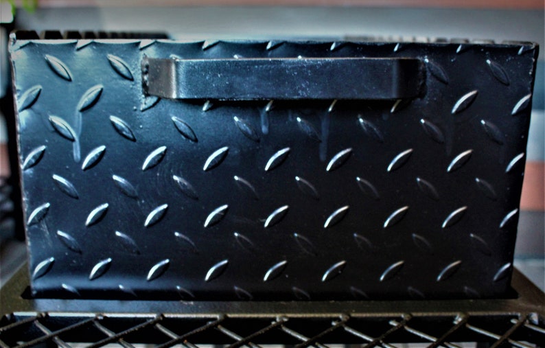 May include: Black metal box with a diamond plate pattern and a black handle. The box is sitting on a black metal frame.