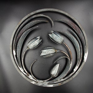 May include: A circular metal wall art piece featuring a design of three stylized tulips with leaves, all in a silver finish.