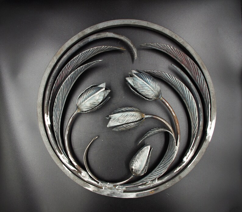 May include: A circular metal wall art piece featuring a design of three stylized tulips with leaves, all in a silver finish.