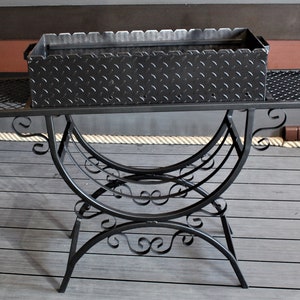 May include: Black metal grill with a diamond plate cooking surface and a decorative wrought iron stand.