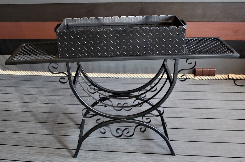 May include: Black metal grill with a diamond plate cooking surface and a decorative wrought iron stand.