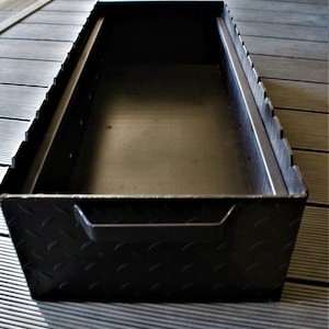 May include: Black metal storage box with a diamond plate pattern on the exterior. The box has a handle on the front and is open to reveal an empty interior.