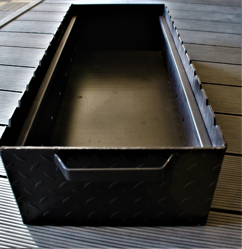 May include: Black metal storage box with a diamond plate pattern on the exterior. The box has a handle on the front and is open to reveal an empty interior.