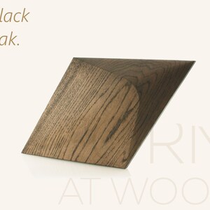 Op de afbeelding: Een geometrisch houten object van zwart eikenhout met een zichtbaar houtnerfpatroon. Het object heeft een schuine, hoekige vorm met een scherpe rand. De tekst "Black oak." staat linksboven en "RMI AT WOOD" staat rechtsonder.