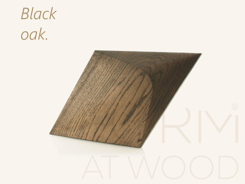 Op de afbeelding: Een geometrisch houten object van zwart eikenhout met een zichtbaar houtnerfpatroon. Het object heeft een schuine, hoekige vorm met een scherpe rand. De tekst "Black oak." staat linksboven en "RMI AT WOOD" staat rechtsonder.