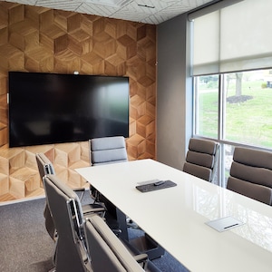 Modern conference room with a geometric wood accent wall featuring 3D wall panels in a natural finish. The textured wall art adds depth and style to the space, serving as both a decorative wood wall panel and a subtle sound diffuser. Perfect example of wall paneling and wood wall decor in office interior design.