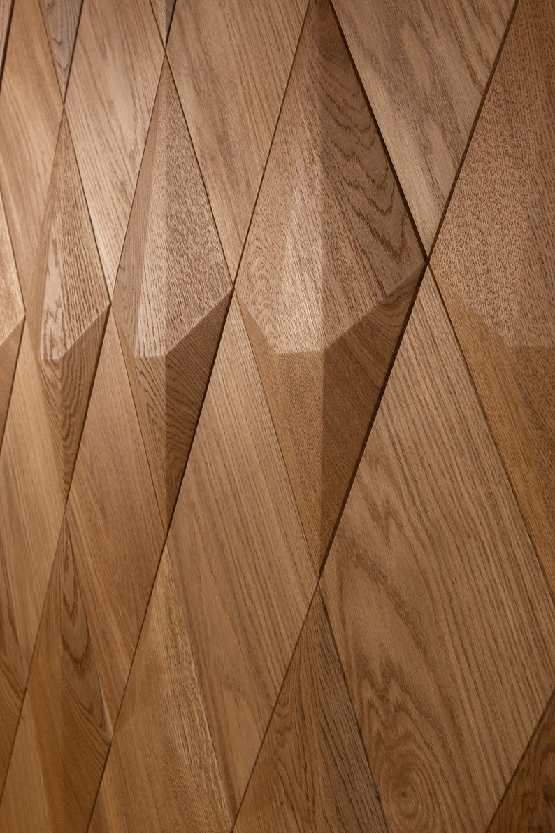 May include: Close-up of a wooden wall panel with a repeating diamond pattern. The panels are made of light brown wood, with visible grain and texture. The geometric design creates a three-dimensional effect, adding depth and visual interest to the surface.