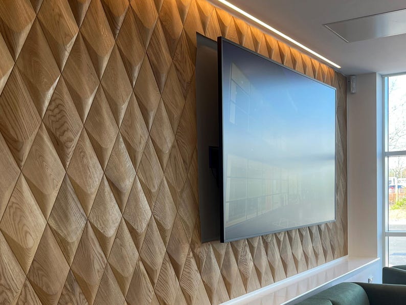 Textured accent wall in a modern interior, featuring 3D wall panels in a diamond pattern made of natural wood. The wall decor surrounds a large TV screen, combining wood wall art with functional design. This wood wall paneling enhances the room’s ambiance with stylish LED lights above, creating a warm and inviting atmosphere. Ideal for living room decor or office wall paneling.