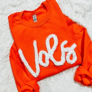 May include: Orange sweatshirt with a white fluffy "Vols" graphic.