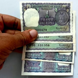 Puede incluir: Un montón de cuatro billetes de una rupia india vintage. Los billetes son verdes y azules con el texto "एक रुपया" (Una rupia) y "ONE RUPEE" impreso en ellos. Los billetes también presentan un retrato de Mahatma Gandhi y el Ashoka Chakra.