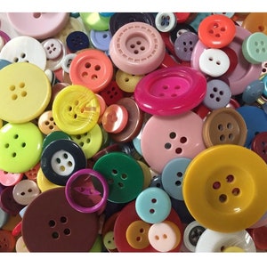 Peut inclure: Un assortiment de boutons colorés de différentes tailles et nuances, notamment jaune, rose, vert et bleu. Les boutons ont deux ou quatre trous et sont en plastique. L'image présente une variété de styles de boutons, des formes rondes simples aux motifs plus décoratifs.
