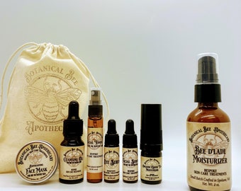 May include: A collection of Botanical Bee Apothecary skincare products. The set includes a face mask, cleansing oil, facial toner, eye serum, facial serum, organic green tea moisturizer, and a Bee D'Lade moisturizer. The products are in small amber bottles and jars, with a drawstring bag.