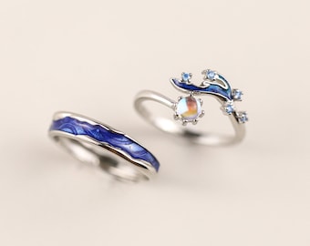 Peut inclure: Deux bagues en argent. L'une présente un motif de vagues en émail bleu. L'autre a un motif de branche en émail bleu avec de petites pierres bleues et une pierre irisée. Bijoux.
