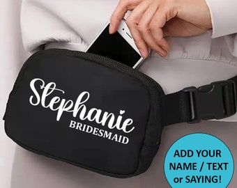 May include: Black fanny pack with a white zipper and a white adjustable strap. The fanny pack has the text "Stephanie Bridesmaid" printed on the front.