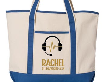 May include: Cream-colored tote bag with blue accents. Features a black graphic of headphones and a sound wave, with the name "RACHEL" and "911 DISPATCHER #34" in gold lettering. The bag has blue handles and a blue bottom.