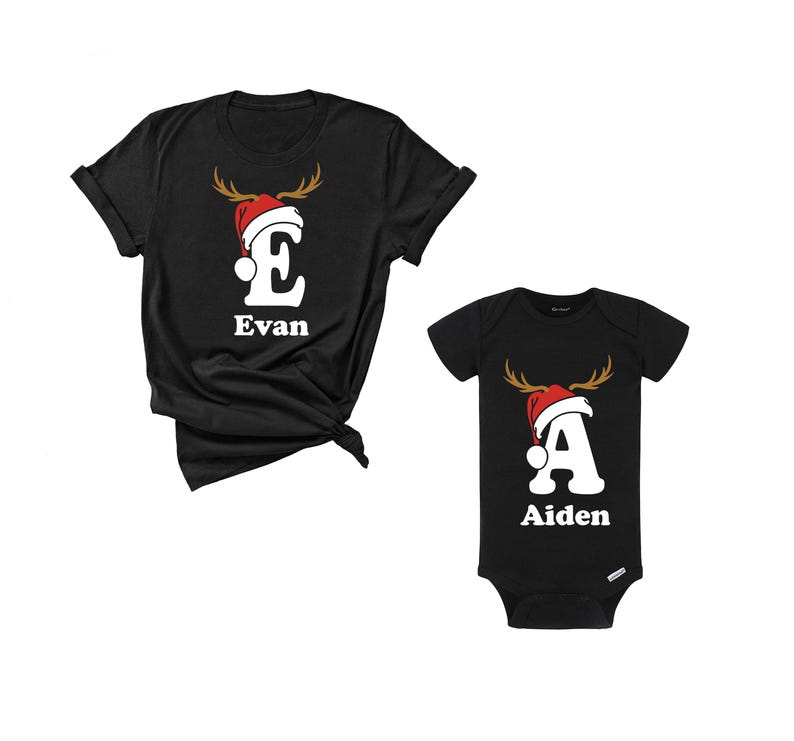 May include: Black t-shirts and a baby onesie with Christmas designs. The t-shirt has a white letter "E" with a reindeer antler design and a Santa hat, with the name "Evan" below. The onesie has a white letter "A" with the same design and the name "Aiden".