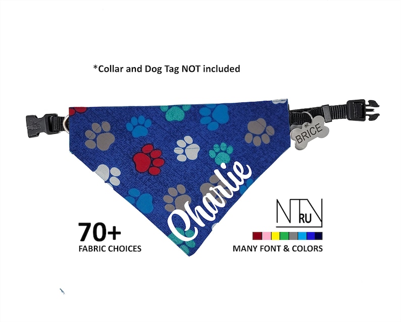 May include: Blue dog bandana with a paw print pattern and the name "Charlie" embroidered in white. The bandana has a black adjustable strap and a silver dog tag that says "BRICE".