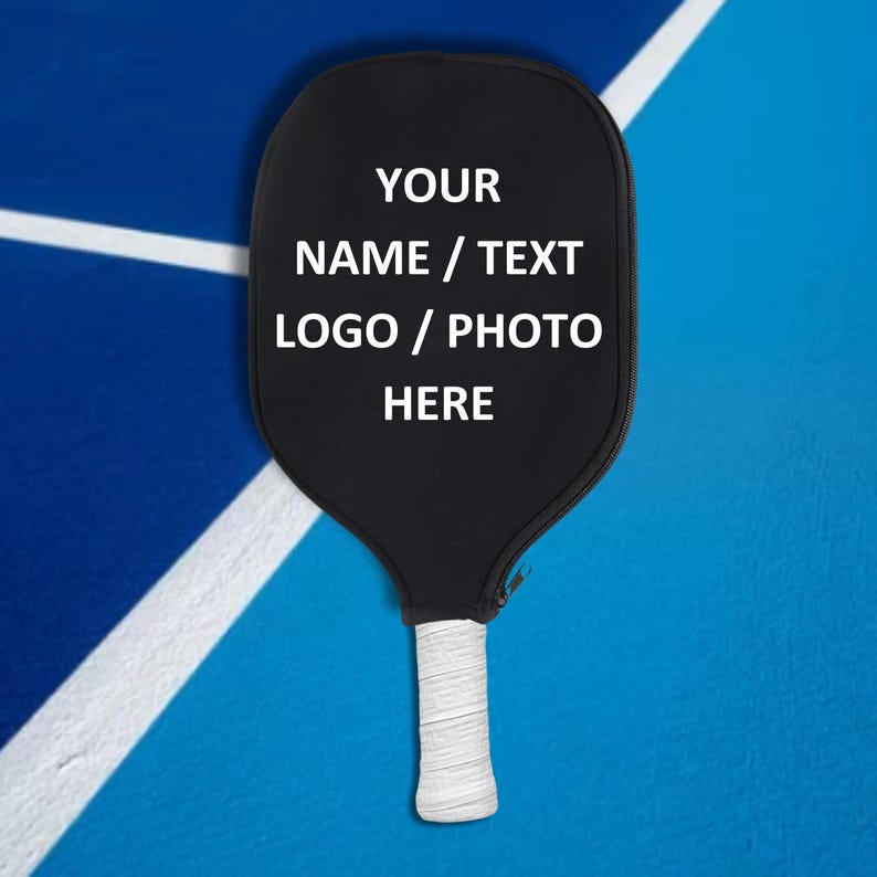 May include: Black pickleball paddle with a white grip. The paddle has white text that says "YOUR NAME / TEXT LOGO / PHOTO HERE".